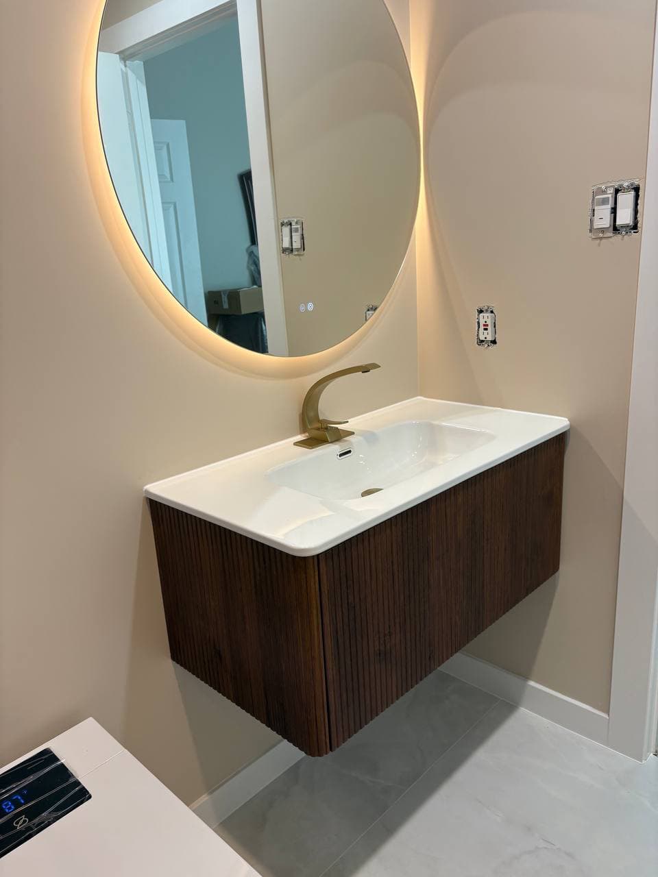 Floating dark wood vanity with gold faucet and backlit mirror