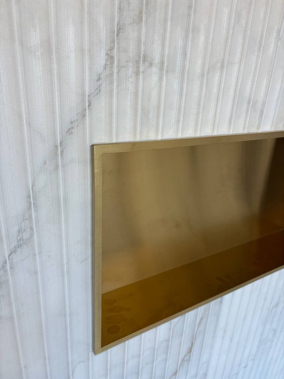 Built-in shower niche with brushed gold frame in white fluted marble tile