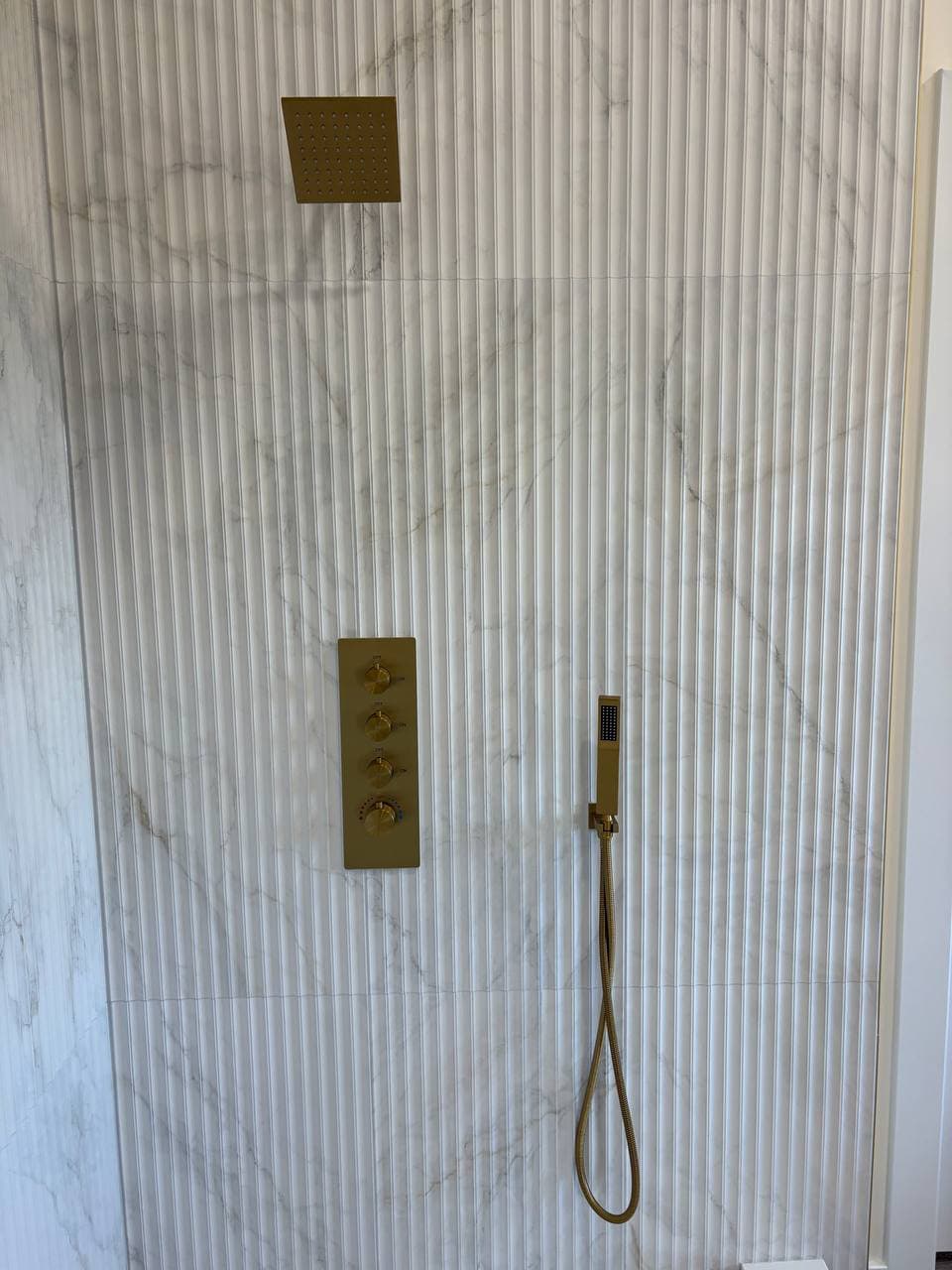 Fluted marble shower wall with gold rain showerhead, thermostatic valve, and handheld