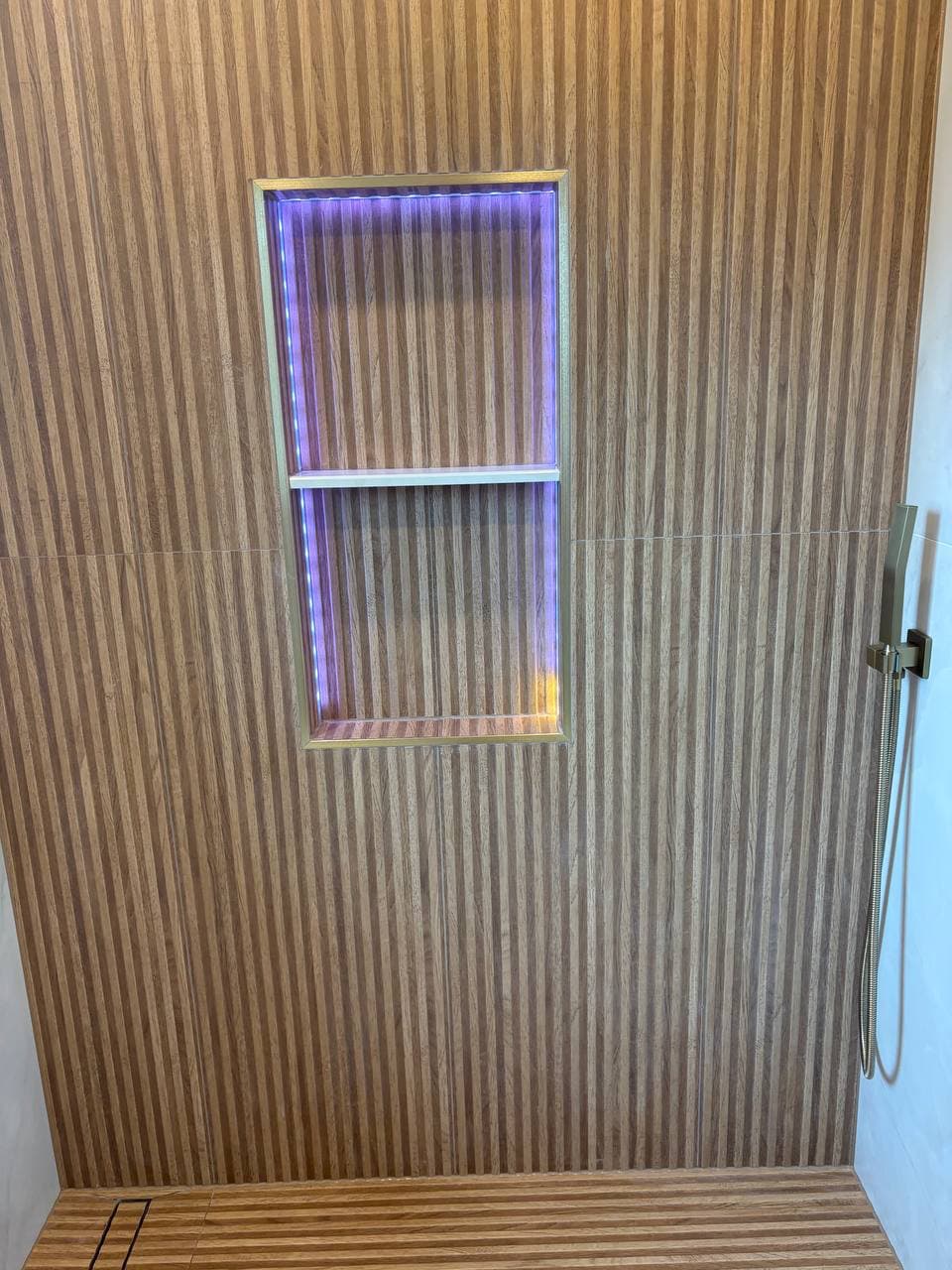 LED-lit niche in wood slat wall with handheld shower hose