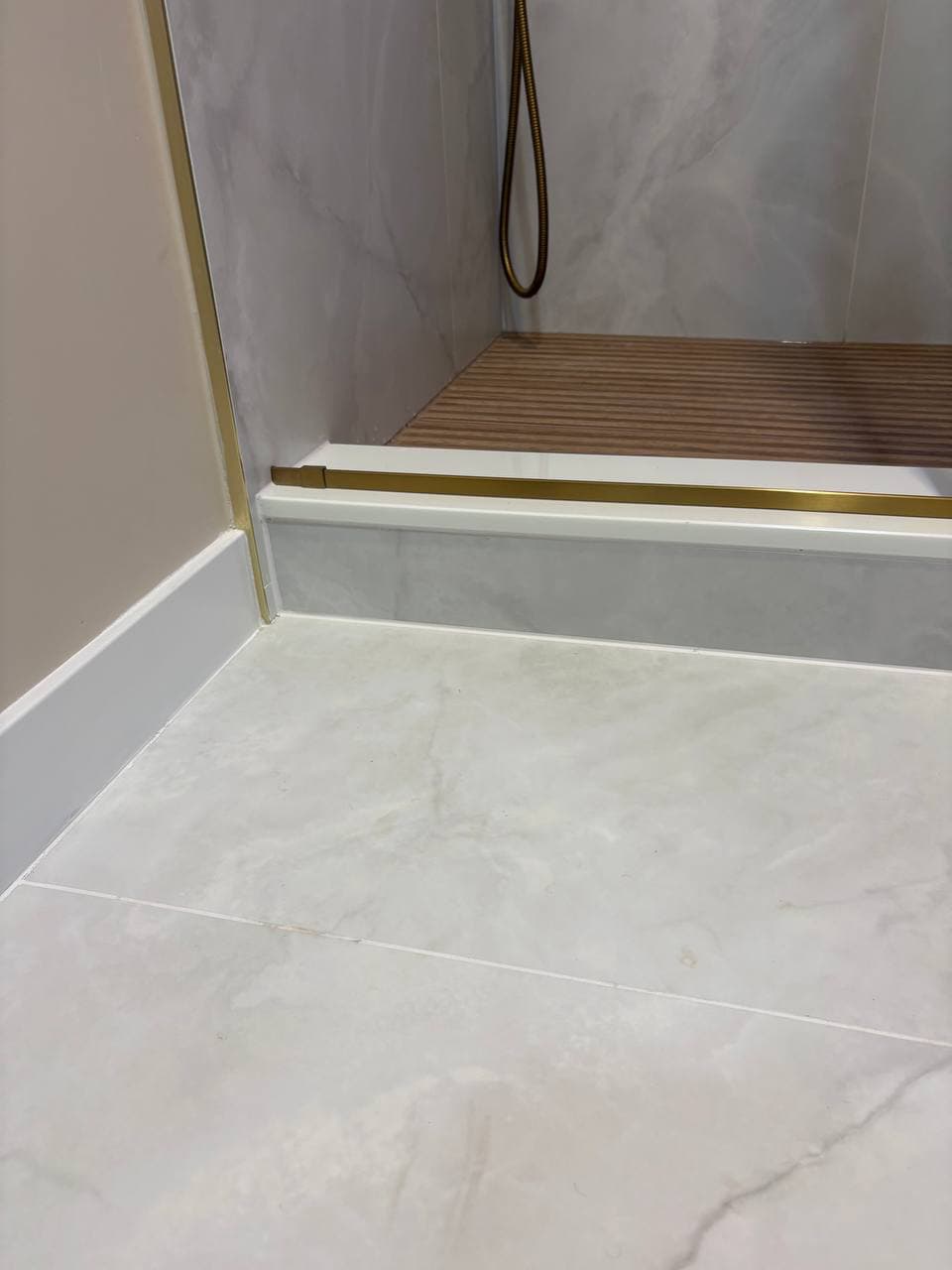 Large format marble floor tiles with gold brass trim at shower curb