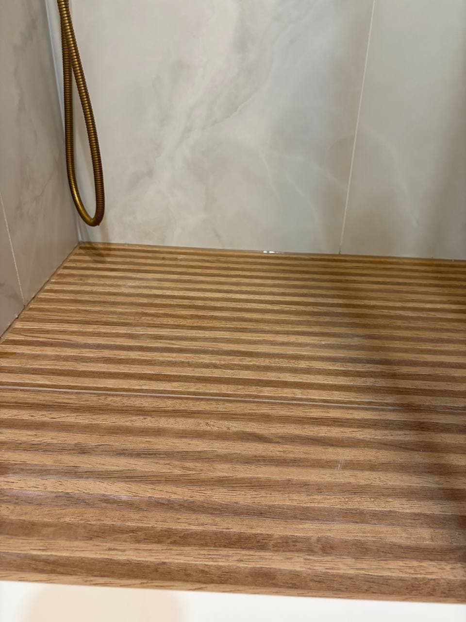 Teak slatted shower floor with gold brass hose and marble walls